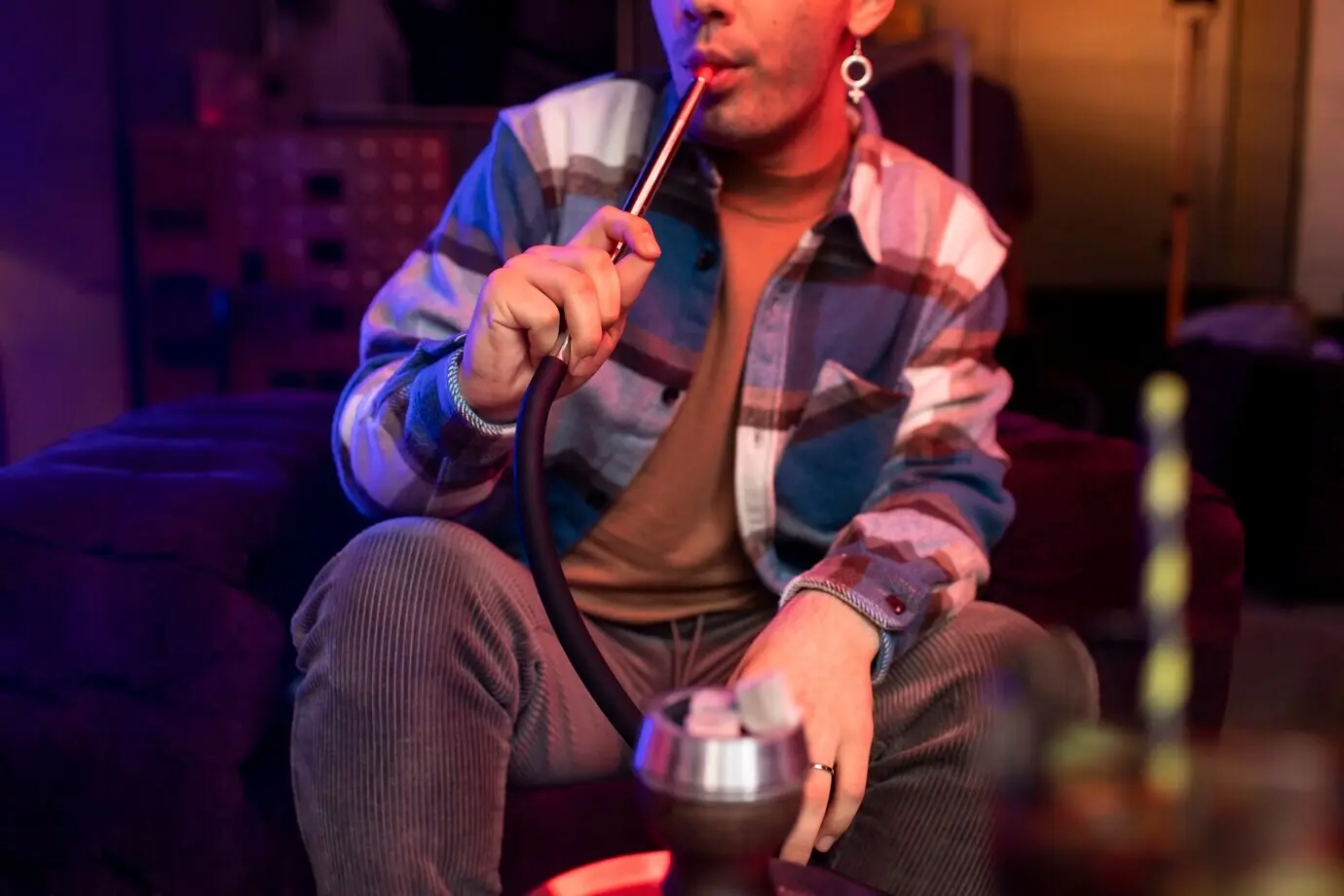 A man inhaling vapor from a hookah indoors.