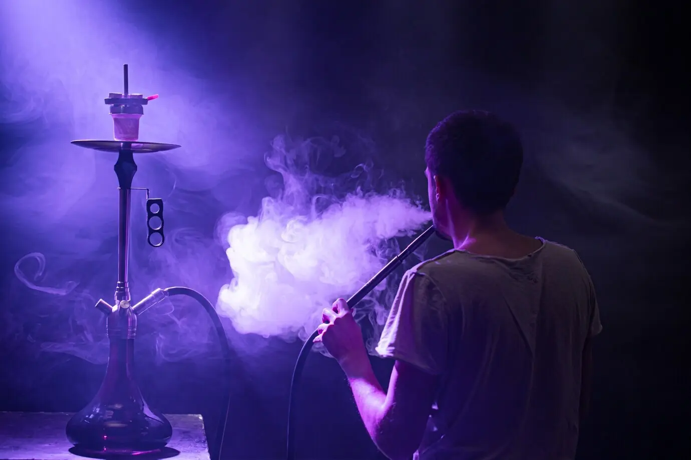 A man smokes a classic shisha, with beautiful colored rays of light and smoke, depicting the concept of hookah smoking.